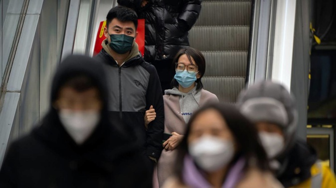 People wearing face masks ride an escalator at a shopping and office complex in Beijing. Photo / AP