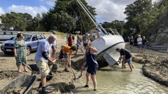 Manly Beach locals dig a channel to try to refloat a yacht washed up by Cyclone Dovi. (Photo / Neville Marriner)