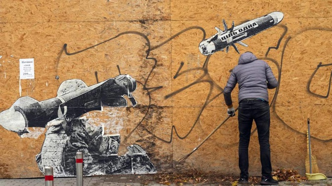 A street cleaner sweeps the autumn leaves near graffiti depicting a Ukrainian soldier firing an anti-tank missile in Kyiv. Photo / Efrem Lukatsky, AP