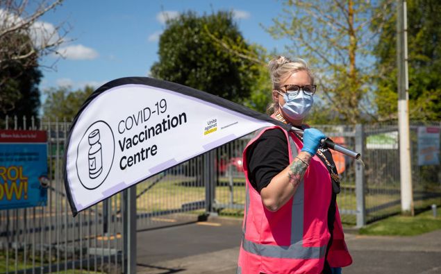 Staff hold signs outside a mobile Covid 19 vaccination centre at Rowandale School, Manurewa. (Photo / Sylvie Whinray)
