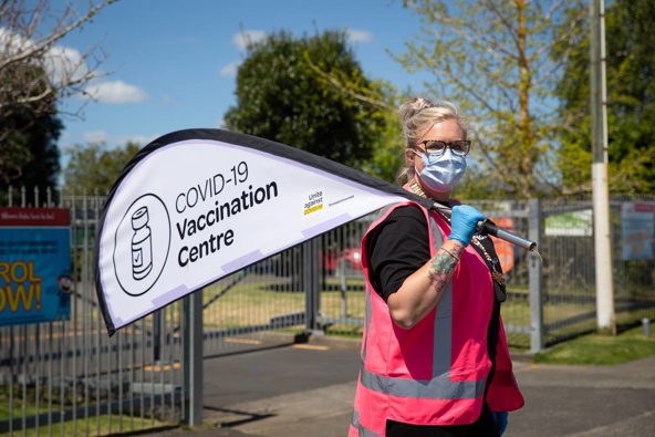 Staff hold signs outside a mobile Covid 19 vaccination centre at Rowandale School, Manurewa. (Photo / Sylvie Whinray)